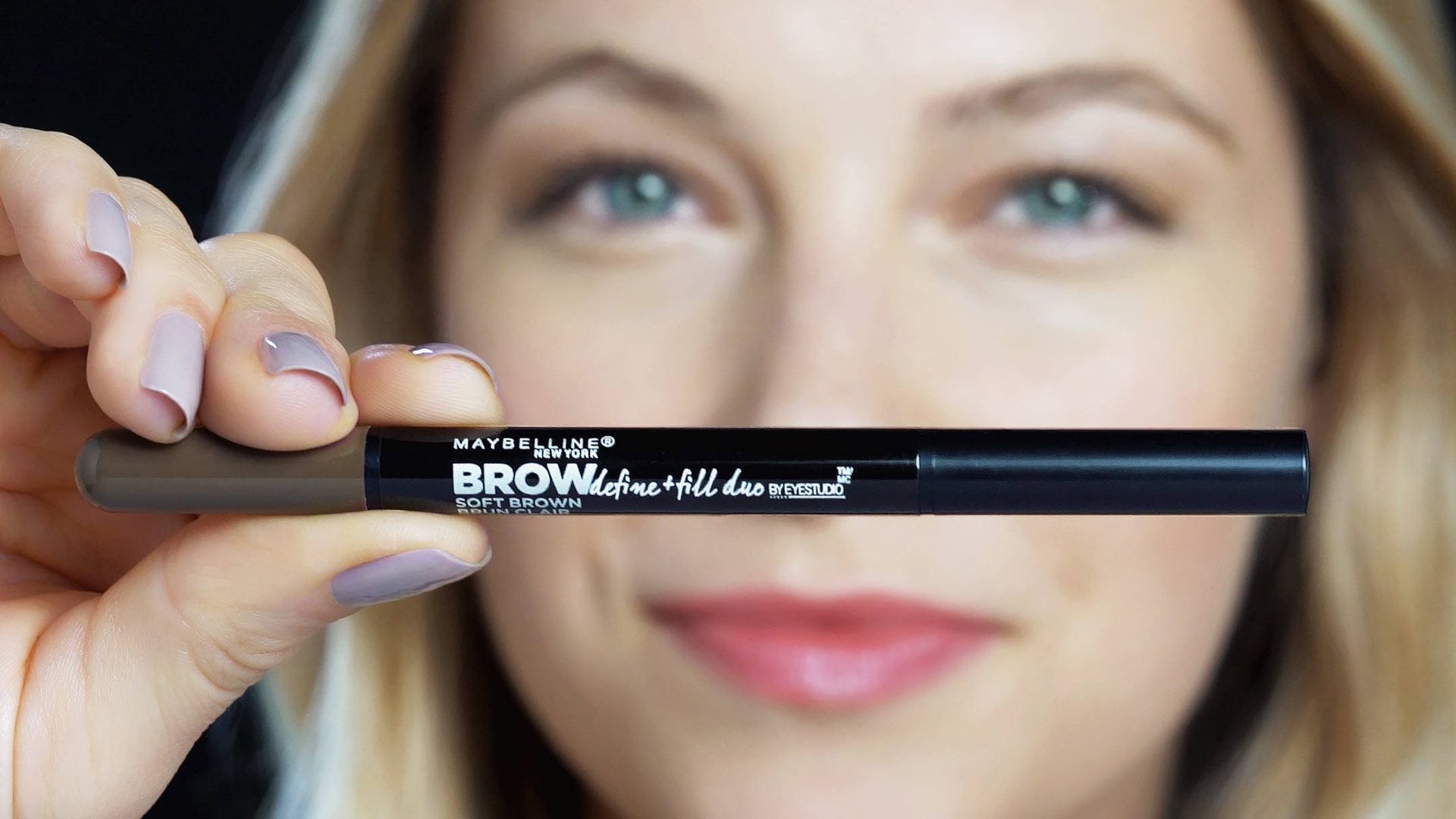 Foco en producto Maybelline de dúo para definir y rellenar las cejas, en la mano de una mujer rubia 